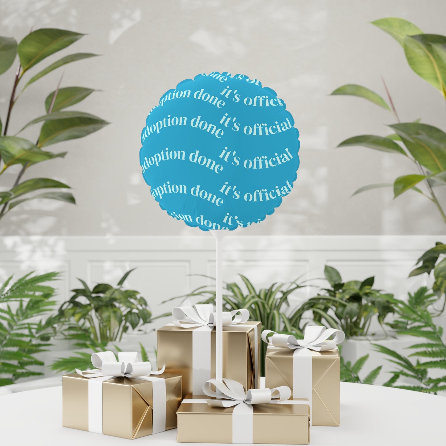 Decorative balloon with 'adoption done, it's official' text in a blue circle, surrounded by gift boxes and plants.